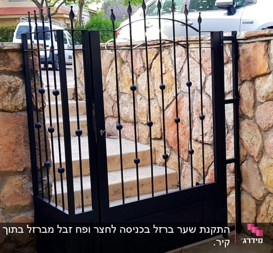 שער מתכת שחור עם עיטורים על רקע קיר אבן